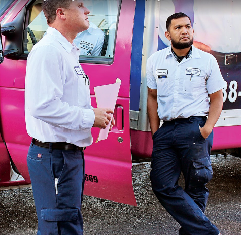 Two Hamilton technicians standing outside their service van, one holding paperwork and the other looking on, both dressed in uniform.