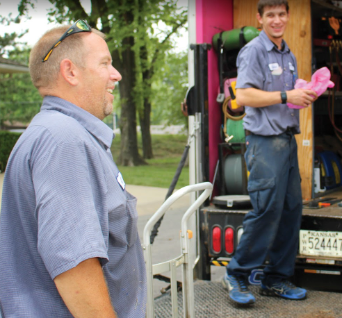 Two Hamilton technicians smiling and preparing equipment from their service truck, one in the foreground and the other in the background.